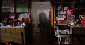Movie still from “Halloween 4: The Return of Michael Myers” (1988), directed by Dwight H. Little – A man standing in the doorway of a store; Wide shot, Low angle