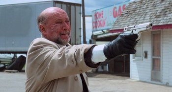 Movie still from “Halloween 4: The Return of Michael Myers” (1988), directed by Dwight H. Little – An older man wearing a trench coat and gloves holding a gun; Medium shot, Low angle