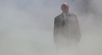 Movie still from “Halloween 4: The Return of Michael Myers” (1988), directed by Dwight H. Little – An older man in a suit and tie standing in the middle of a foggy street; Wide shot, Low angle