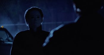 Movie still from “Halloween 4: The Return of Michael Myers” (1988), directed by Dwight H. Little – A person with a mask is standing in the dark; Close Up shot, Over the shoulder angle