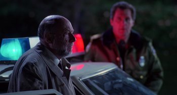Movie still from “Halloween 4: The Return of Michael Myers” (1988), directed by Dwight H. Little – A man in a trench coat standing next to another man in front of a car; Medium shot, Low angle