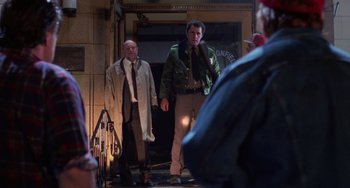 Movie still from “Halloween 4: The Return of Michael Myers” (1988), directed by Dwight H. Little – Two men are standing in front of a building; Wide shot, Low angle