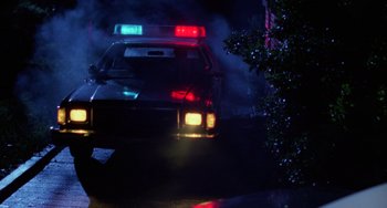 Movie still from “Halloween 4: The Return of Michael Myers” (1988), directed by Dwight H. Little – A police car is lit up at night with fog; Wide shot, Low angle