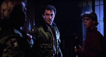 Movie still from “Halloween 4: The Return of Michael Myers” (1988), directed by Dwight H. Little – A man in a green jacket standing next to a wall; Medium shot, Over the shoulder angle