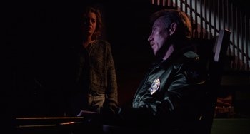 Movie still from “Halloween 4: The Return of Michael Myers” (1988), directed by Dwight H. Little – A man and a woman are sitting in a dark room; Medium shot, Low angle