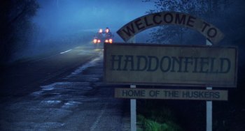 Movie still from “Halloween 4: The Return of Michael Myers” (1988), directed by Dwight H. Little – A car driving down a road next to a welcome sign; Extreme Wide shot, Low angle