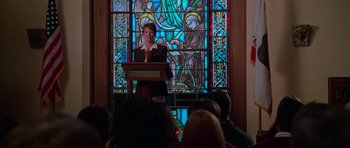 Movie still from “Halloween H20: 20 Years Later” (1998), directed by Steve Miner – A person is standing at a podium in front of a stained glass window; Medium shot, Low angle