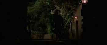 Movie still from “Halloween H20: 20 Years Later” (1998), directed by Steve Miner – A man walking in the dark near some bushes; Wide shot, Low angle