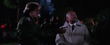 Movie still from “Halloween II” (1981), directed by Rick Rosenthal – A man smoking a cigarette next to another man in a trench coat; Medium shot, Over the shoulder angle