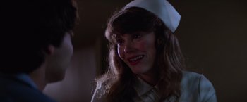 Movie still from “Halloween II” (1981), directed by Rick Rosenthal – A woman wearing a nurse's hat and smiling for the camera; Close Up shot, Over the shoulder angle