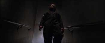 Movie still from “Halloween II” (1981), directed by Rick Rosenthal – A man with a mask is standing in a dark room; Medium shot, Low angle