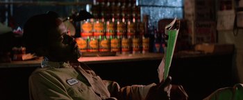 Movie still from “Halloween III: Season of the Witch” (1982), directed by Tommy Lee Wallace – A man sitting in front of a shelf with bottles of alcohol; Close Up shot, Low angle