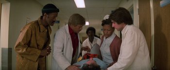 Movie still from “Halloween III: Season of the Witch” (1982), directed by Tommy Lee Wallace – A group of people standing next to a patient; Medium shot, Low angle