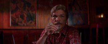 Movie still from “Halloween III: Season of the Witch” (1982), directed by Tommy Lee Wallace – A man sitting in front of a window holding a glass of water; Close Up shot, Low angle