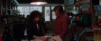 Movie still from “Halloween III: Season of the Witch” (1982), directed by Tommy Lee Wallace – A man and a woman are looking at a book together; Medium shot, Over the shoulder angle