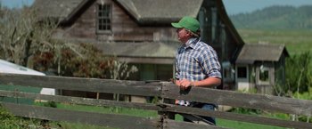 Movie still from “Halloween III: Season of the Witch” (1982), directed by Tommy Lee Wallace – A man wearing a green hat standing next to a wooden fence; Medium shot, Over the shoulder angle