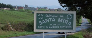 Movie still from “Halloween III: Season of the Witch” (1982), directed by Tommy Lee Wallace – A sign that reads " welcome to santa maria " on the side of the road; Wide shot, High angle