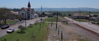 Movie still from “Halloween III: Season of the Witch” (1982), directed by Tommy Lee Wallace – An aerial view of an empty road with a train station in the background; Extreme Wide shot, High angle