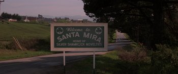 Movie still from “Halloween III: Season of the Witch” (1982), directed by Tommy Lee Wallace – A sign that reads " welcome to santa mira " on the side of the road; Wide shot, High angle