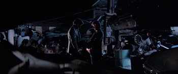 Movie still from “Halloween III: Season of the Witch” (1982), directed by Tommy Lee Wallace – Two people standing in a dark room talking to each other; Wide shot, Over the shoulder angle