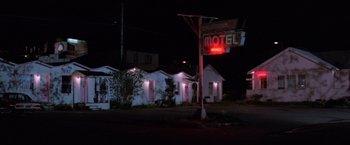 Movie still from “Halloween III: Season of the Witch” (1982), directed by Tommy Lee Wallace – A motel sign lit up at night in the dark; Wide shot, Low angle