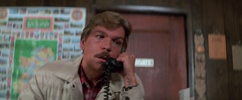 Movie still from “Halloween III: Season of the Witch” (1982), directed by Tommy Lee Wallace – A man with a mustache talking on a phone; Close Up shot, Low angle