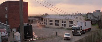 Movie still from “Halloween III: Season of the Witch” (1982), directed by Tommy Lee Wallace – A car is parked in a parking lot near a building; Extreme Wide shot, High angle