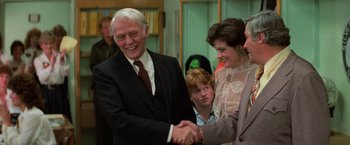 Movie still from “Halloween III: Season of the Witch” (1982), directed by Tommy Lee Wallace – A man and a woman shaking hands in front of a crowd; Medium shot, Over the shoulder angle
