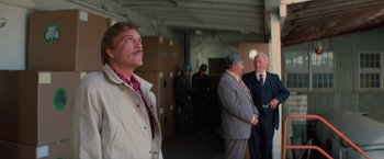 Movie still from “Halloween III: Season of the Witch” (1982), directed by Tommy Lee Wallace – A group of men standing next to each other in a room; Medium shot, Over the shoulder angle