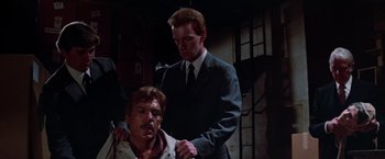 Movie still from “Halloween III: Season of the Witch” (1982), directed by Tommy Lee Wallace – A man in a suit and tie is standing next to another man in a suit and tie; Medium shot, Low angle