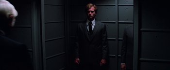 Movie still from “Halloween III: Season of the Witch” (1982), directed by Tommy Lee Wallace – A man in a suit and tie standing in a dark room; Medium shot, Low angle