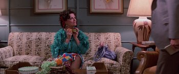 Movie still from “Halloween III: Season of the Witch” (1982), directed by Tommy Lee Wallace – A woman sitting on top of a couch eating a hamburger; Medium shot, High angle