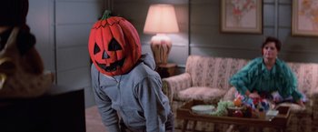 Movie still from “Halloween III: Season of the Witch” (1982), directed by Tommy Lee Wallace – A person wearing a pumpkin mask in a living room; Close Up shot, High angle