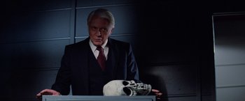 Movie still from “Halloween III: Season of the Witch” (1982), directed by Tommy Lee Wallace – A man in a suit and tie next to a human skull; Close Up shot, Over the shoulder angle