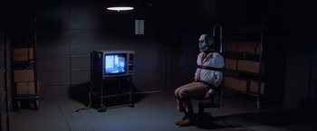 Movie still from “Halloween III: Season of the Witch” (1982), directed by Tommy Lee Wallace – A man sitting in front of a tv in a room; Wide shot, High angle