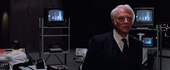 Movie still from “Halloween III: Season of the Witch” (1982), directed by Tommy Lee Wallace – A man in a suit and tie sitting in front of a tv; Close Up shot, Over the shoulder angle