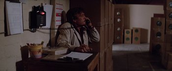 Movie still from “Halloween III: Season of the Witch” (1982), directed by Tommy Lee Wallace – A man sitting at a desk talking on the phone; Medium shot, Over the shoulder angle