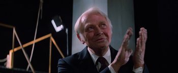 Movie still from “Halloween III: Season of the Witch” (1982), directed by Tommy Lee Wallace – An older man wearing a suit and tie clapping his hands; Close Up shot, Low angle
