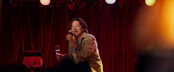 Movie still from “Halloween Kills” (2021), directed by David Gordon Green – A man standing on a stage holding a microphone; Medium shot, Over the shoulder angle