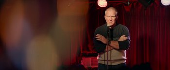 Movie still from “Halloween Kills” (2021), directed by David Gordon Green – A man standing on a stage holding a microphone; Medium shot, Over the shoulder angle