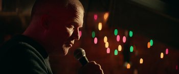 Movie still from “Halloween Kills” (2021), directed by David Gordon Green – A man with a shaved head is holding a microphone; Close Up shot, Over the shoulder angle