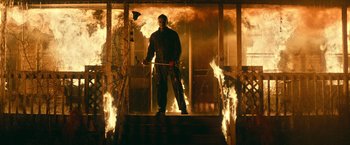 Movie still from “Halloween Kills” (2021), directed by David Gordon Green – A man holding a baseball bat in front of a fire; Wide shot, Low angle