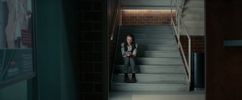 Movie still from “Halloween Kills” (2021), directed by David Gordon Green – A woman sitting on the stairs looking at her cell phone; Wide shot, High angle