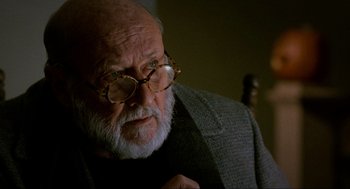 Movie still from “Halloween: The Curse of Michael Myers” (1995), directed by Joe Chappelle – An old man with a beard wearing glasses and a jacket; Close Up shot, Over the shoulder angle