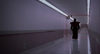 Movie still from “Halloween: The Curse of Michael Myers” (1995), directed by Joe Chappelle – A person walking down a long hallway with a fan; Wide shot, Over the shoulder angle