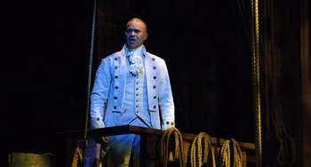 Movie still from “Hamilton” (2020), directed by Thomas Kail – A man in a white suit standing in front of ropes; Medium shot, Low angle