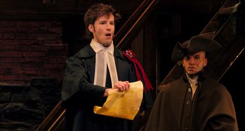Movie still from “Hamilton” (2020), directed by Thomas Kail – A man holding a piece of paper in front of another man; Medium shot, High angle