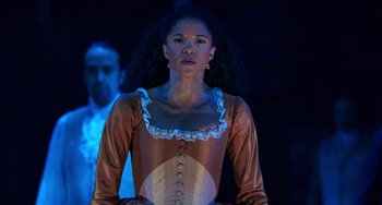 Movie still from “Hamilton” (2020), directed by Thomas Kail – A woman in a brown and white dress standing next to a man; Medium shot, Over the shoulder angle
