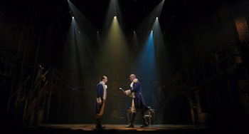 Movie still from “Hamilton” (2020), directed by Thomas Kail – Two men in blue and white uniforms on a stage; Wide shot, Low angle