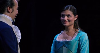 Movie still from “Hamilton” (2020), directed by Thomas Kail – A woman in a blue dress standing in front of a black background; Close Up shot, High angle